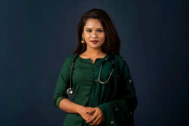 A smiling female doctor wearing a stethoscope on her shoulders looking at the camera on gray background.