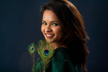Beautiful Young Girl posing with peacock feathers on grey background.