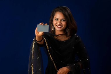 Young smiling beautiful girl posing with a credit or debit card on blue background.