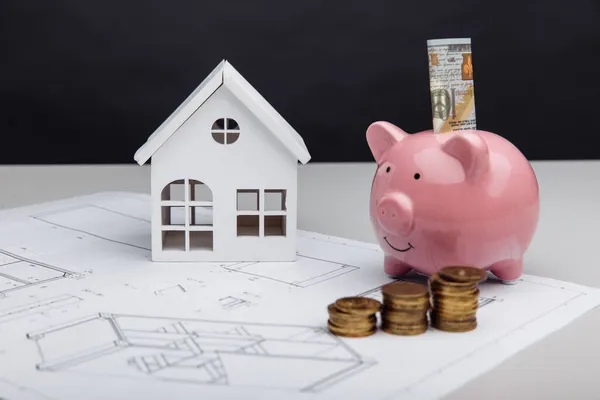 Model domu i skarbonki z dolarem i monetami na planie architektonicznym. Koszty budowy domów — Zdjęcie stockowe