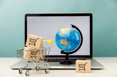 Çevrimiçi alışveriş ve ecommerce konsepti. Küresel ve süpermarket alışveriş arabaları dizüstü bilgisayarın yanında kutular