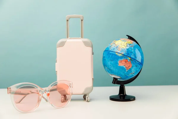 Tourism concept. Plastic travel suitcase, pink glasses and globe