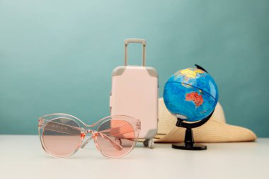 Turizm fikri. Plastik seyahat valizi, pembe gözlükler ve masanın üzerindeki küre.