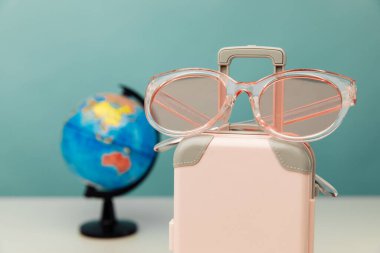 Seyahat teması. Plastik seyahat valizi, pembe gözlük ve küre yakın plan bir masada.
