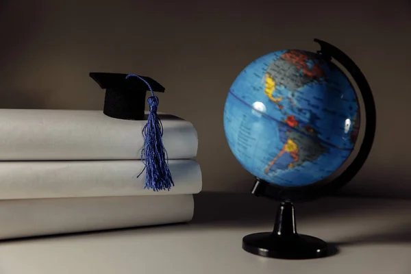 Student absolvent care studiază în străinătate idee internațională. Pălărie de absolvire și glob pe o masă — Fotografie, imagine de stoc