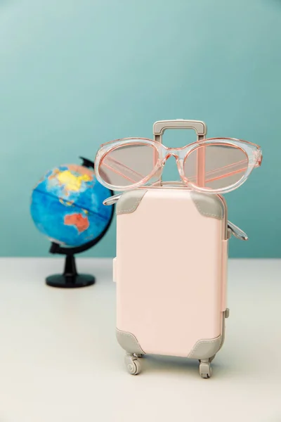 Conceito de turismo. Mala de viagem de plástico, óculos rosa e globo. Imagem vertical — Fotografia de Stock