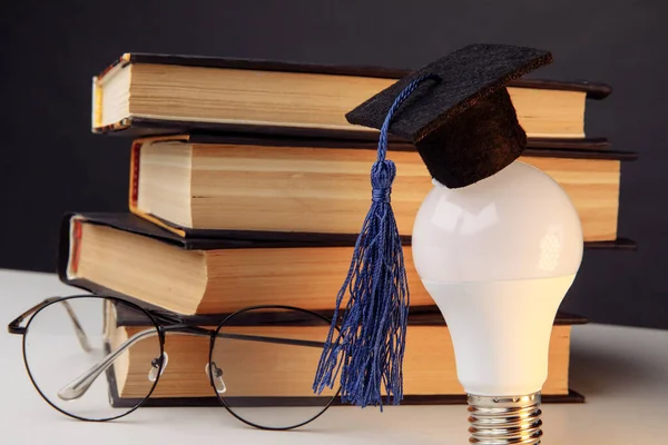 Graduation hat on light bulb with books on a white table. Education and science concept — Stock Photo, Image