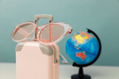 Plastik seyahat valizi, pembe gözlükler ve yakın plan dünya fotoğrafı. Seyahat planlama kavramı