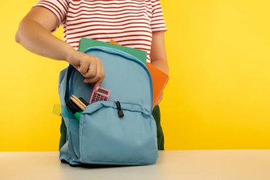 Farklı renkte kırtasiyelerle dolu sırt çantası taşıyan genç bir kız, sarı renkte izole edilmiş.