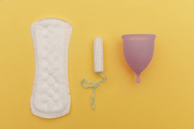 Pad, regl kupası ve sarı arka planda tampon. Kritik günler ve hijyen kavramı