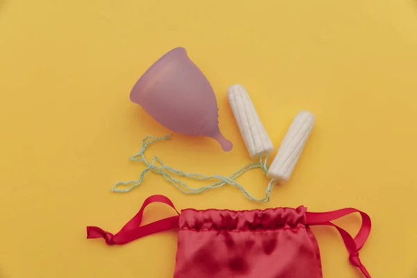 Herbruikbare pastelpaarse menstruatiecup en tampons op een gele achtergrond. Vrouwenhygiëne, menstruatie, kritieke dagen — Stockfoto