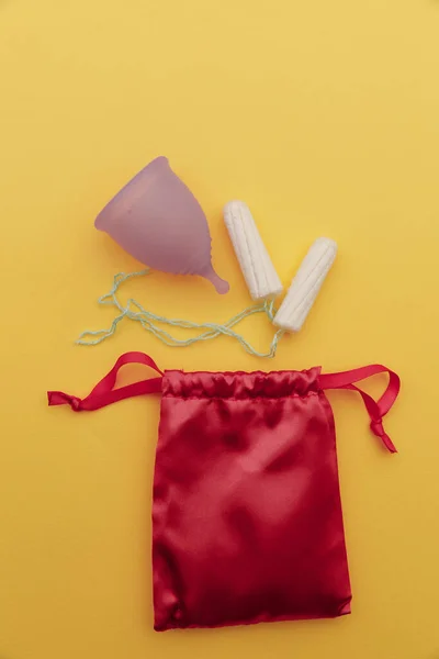 Tazza mestruale viola pastello riutilizzabile e tamponi su sfondo giallo. Igiene delle donne, mestruazioni, giorni critici. Immagine verticale — Foto Stock