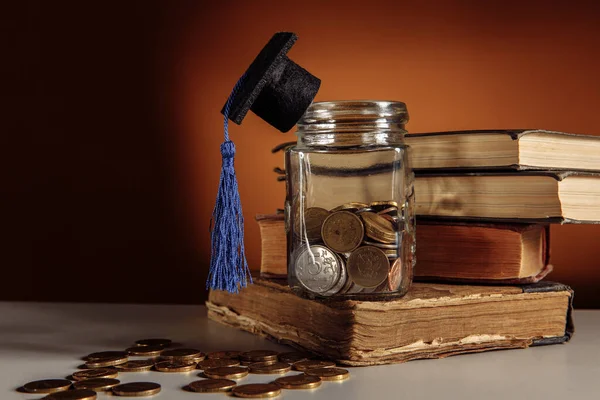 Glazen pot met munten en afstudeerhoed op tafel, beursconcept — Stockfoto