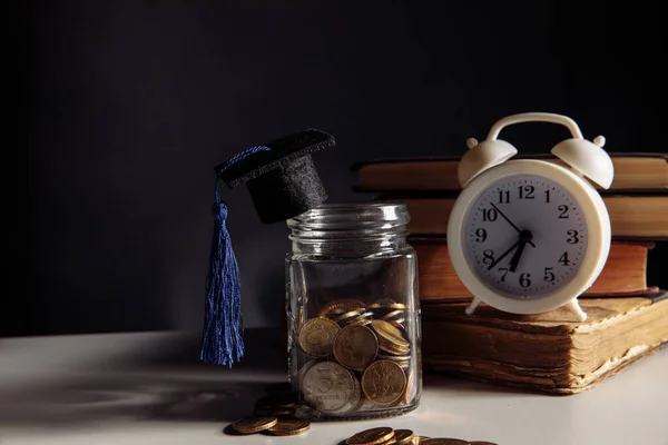 Sombrero de graduación en tarro con monedas y reloj despertador en un aula Fotos De Stock Sin Royalties Gratis