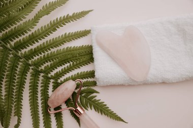 Güzellik konsepti. Gua sha ve masaj silindiri bir havluda ve eğreltiotu pembe arka planda
