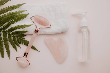 Şişede ve silindirde esans, pembe arka planda gua sha masaj kazıyıcısı. Üst Manzara. Bencillik, güzellik ve sağlık konsepti