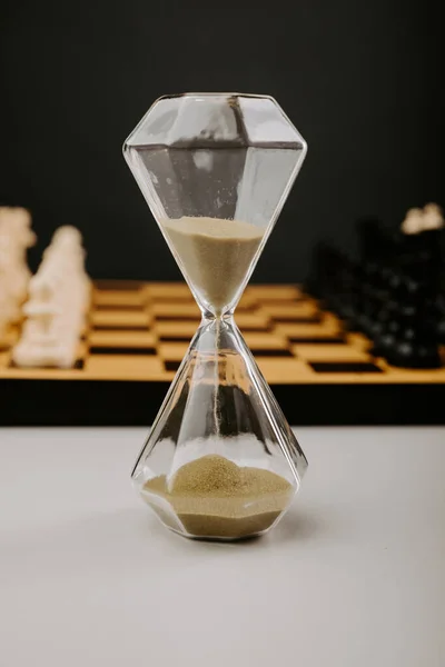 Reloj de arena y piezas de ajedrez sobre fondo gris. Concepto deportivo y de ocio. Imagen vertical —  Fotos de Stock