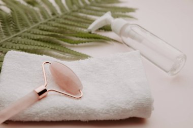 Havlu ve pembe arka planda eğrelti otu yaprağı olan güzellik ürünü.