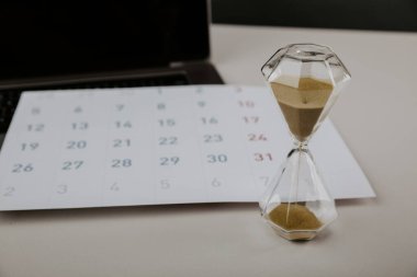 Takvim ve dizüstü bilgisayarlı bir masaüstü kum saati, yıl değişimi veya son teslim tarihi kavramı