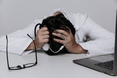 Depresyonda olan erkek doktor masadaki steteskopla tıbbi muayenehanede yatıyor. Yanma konsepti