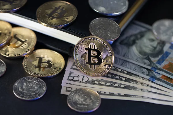 Defterin üstünde Bitcoin ve Amerikan Doları banknotları. Yarım Dolarlık madeni paralar ve Amerikan banknotları
