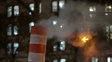 Steam coming from pipe and chimney at Night in NYC. Traffic light blinking in background behind fog in Manhattan