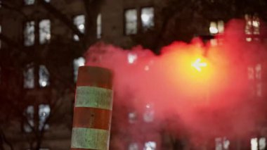 Steam coming from pipe and chimney at Night in NYC. Traffic light red in background behind fog in Manhattan
