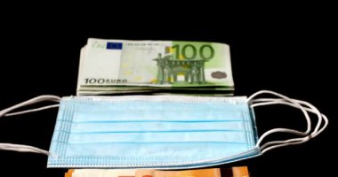 Yüz maskelerinin yanına yığılmış Euro banknotları. Maskeler ve Covid-19 'a karşı koruma maliyeti. Ekonomik salgın