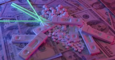 Üstüne beyaz haplar yığılmış ve Amerikan dolarları etrafa saçılmış. İlaç tabletlerinin üstündeki test kiti.