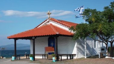 Tepedeki Yunan Kilisesi, arka plandaki Agean Denizi. Küçük kilisenin üzerinde Yunan bayrağı dalgalanır. Yunanistan 'da Tatil