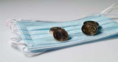 Beyaz yüzeyinde Avrupa sikkeleri olan Mavi Yüz Maskesi. Cerrahi Maskenin Üstüne İki Euro Bozuk Para