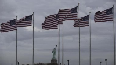 Arka planda Flag Plaza ve Özgürlük Heykeli var. ABD bayrakları ağır çekimde dalgalanıyor. Amerika Birleşik Devletleri bayrakları