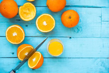 Bıçak portakalı ikiye bölüyor, birkaç organik portakaldan oluşan bir bardak, bazıları diyet için sıkılmış, mavi ahşap bir masada, sağlıklı bir kahvaltı.