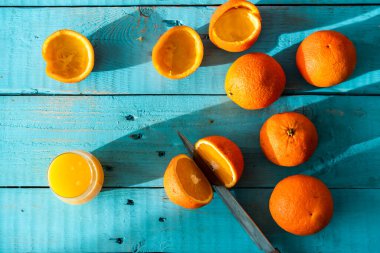 Bıçakla birkaç portakal biyo 'sunu keserken, bazıları sıkılmış, mavi ahşap bir masada doğal meyve suyu yapmak için. Sağlıklı kahvaltı.