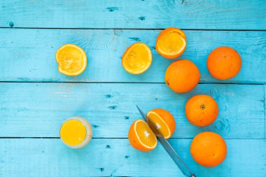 Bıçakla birkaç portakal biyo 'sunu keserken, bazıları sıkılmış, mavi ahşap bir masada doğal meyve suyu yapmak için. Sağlıklı kahvaltı.