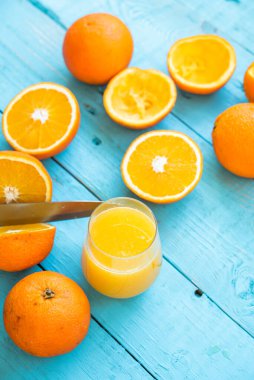 Bıçak portakalı ikiye bölüyor, birkaç organik portakaldan oluşan bir bardak, bazıları diyet için sıkılmış, mavi ahşap bir masada, sağlıklı bir kahvaltı.