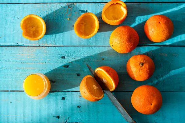 Bıçakla birkaç portakal biyo 'sunu keserken, bazıları sıkılmış, mavi ahşap bir masada doğal meyve suyu yapmak için. Sağlıklı kahvaltı.