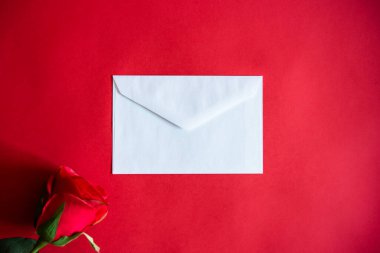 Kırmızı arka planda beyaz bir zarf, Sevgililer Günü 'nde eşinize bir aşk mektubu yazmak için, ya da fethetmek için, ve bir gül ile, sevginin sembolü. Aşk kavramı