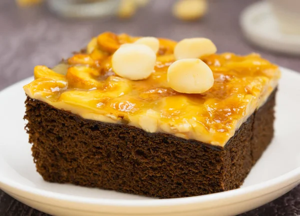 Close up toffee chocolate cake slice with macadamia seeds above on plate on stone background for dessert break. Toffee cake made from bake, dark chocolate, macadamia, nut, caramel