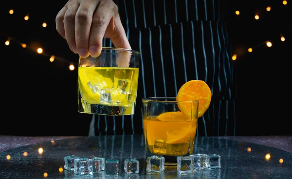 男はオレンジジュースグラスの上に新鮮なレモンジュースグラスリムを持ち上げ テーブルの上に氷 バーテンダーはバーでパーティーで飲むためのフルーツカクテルや新鮮なジュースを準備します — ストック写真