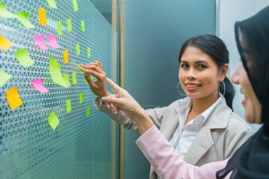 İş kadınları iş yerindeki ve toplantı salonundaki aynaya yapışmış post-it yapıştırırken mutlu bir gülümseme sergiliyorlar. Profesyonel iş adamı ofiste çalışmakla meşgul.