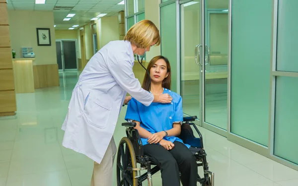 Doktor kadınlar hastanede tekerlekli sandalyede oturan hasta kadınların nefeslerini kontrol ediyorlar. Steteskoplu doktor hastanedeki hastanın sağlığını kontrol ediyor.