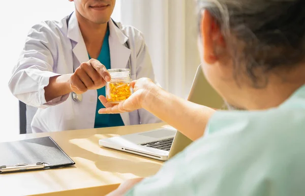 Odaklanan ilaç kapsülü, doktor ilaç kapsülü veriyor ve yaşlı hasta adama bakıyor. Doktor ya da hemşire yaşlı hasta sağlığı ziyaretleriyle ilgilenir.