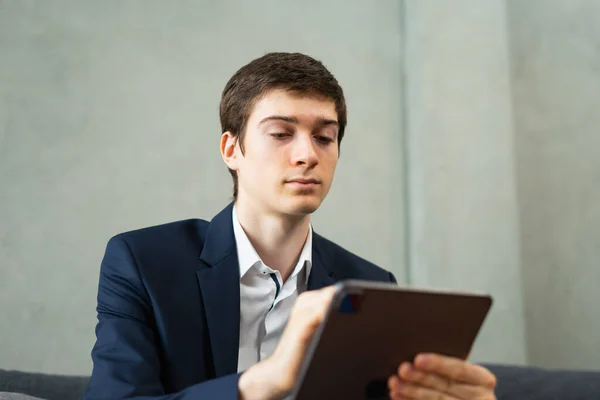 Kafkas iş adamının solucana bakış açısı ciddi şekilde tabletle çalışıyor, takım elbise giyiyor, oturuyor, tablete bakıyor, arka plandaki boşluğu kopyalıyor. Genç adam ofis geçmişi ve fotokopi alanı olan bir işte çalışıyor.