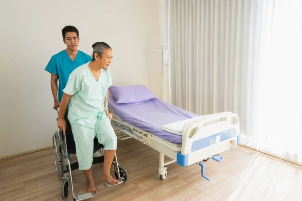 Yaşlı hasta tekerlekli sandalyeden yatağa. Doktor ya da hemşire yaşlı hasta sağlığı kabulüyle ilgilenir.