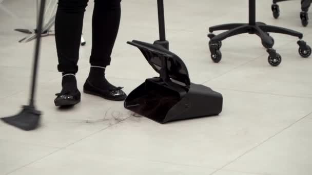 Жінка в чорному одязі видаляє волосся з підлоги в перукарні — стокове відео