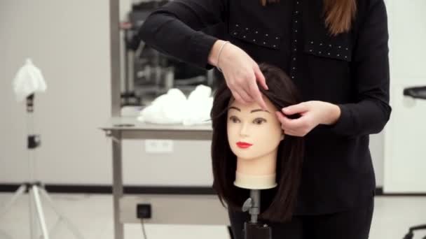 Una ragazza in abiti neri taglia i capelli di un manichino — Video Stock