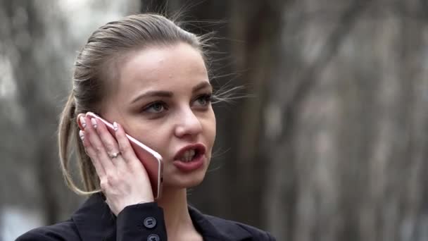 Ung vit tjej i svart jacka pratar i telefon i en stadspark — Stockvideo