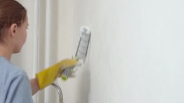 Beyaz kız duvarları silindirle boyuyor. 