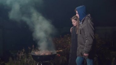 Kız barbeküyü kızartır ve ateşi körükler.